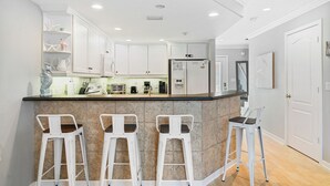 Una cocina moderna con armarios blancos, una isla central con taburetes y un refrigerador.