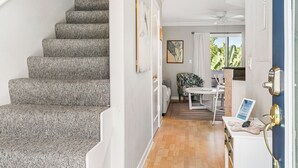 Una escalera con peldaños cubiertos de moqueta gris que conduce a una habitación con piso de madera, un ventilador de techo y vistas al exterior de zonas verdes.