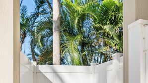 Un portón de madera blanca que da a un espacio exterior cubierto con suelo de concreto y vegetación.