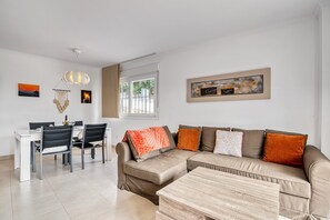 A modern living room with a sofa, dining table, chairs, and a hanging light fixture.