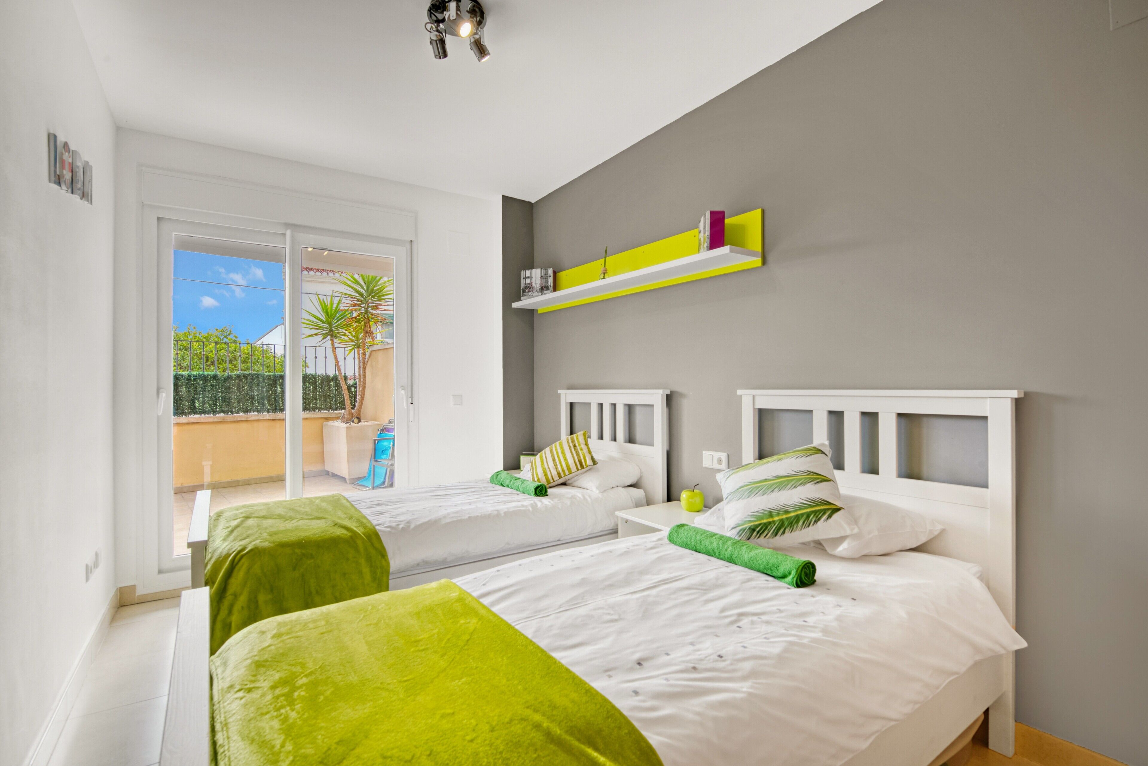 A hotel room with two beds, a balcony with a view, and a shelf with books.