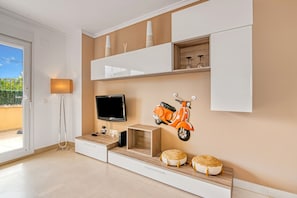 A modern living room with a flat-screen TV, a wall-mounted scooter decoration, and a sliding door leading to an outdoor area.