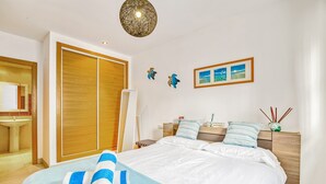 A hotel room with a bed, a wooden wardrobe, a bedside table with a lamp, and a wall-mounted picture. - Holiday Apartment "Amanda" with Mountain View, Shared Pool & Wi-Fi (Xàbia)