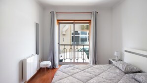 Une chambre à coucher comprenant un lit, une table de chevet, une lampe, un radiateur, une fenêtre avec des rideaux et une vue sur l’extérieur.