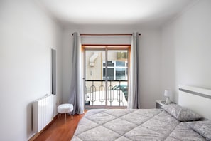 Une chambre à coucher comprenant un lit, une table de chevet, une lampe, un radiateur, une fenêtre avec des rideaux et une vue sur l’extérieur.