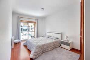 Une chambre à coucher comprenant un lit, des tables de chevet, une commode, une fenêtre avec des rideaux, un balcon et une porte.