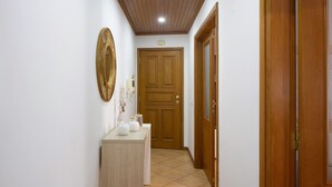Un couloir avec une porte en bois, une petite armoire contenant des objets décoratifs et un miroir fixé au mur.