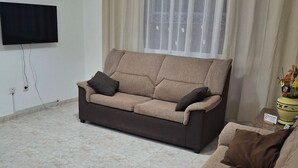 A living room with a sofa, a smaller couch, a flat-screen TV, a window with curtains, and a tiled floor. - Holiday Home "Casa Rosi" with Mountain Views and Wi-Fi (Gran Tarajal)