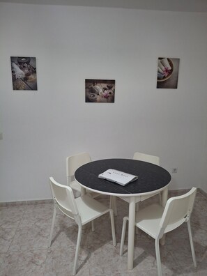 A room with a round table, four chairs, and two framed pictures on the wall.