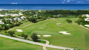 A golf course with sand bunkers, a well-maintained fairway, and a view of the ocean.