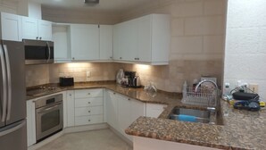 A compact kitchen with white cabinets, stainless steel appliances, and a granite countertop.