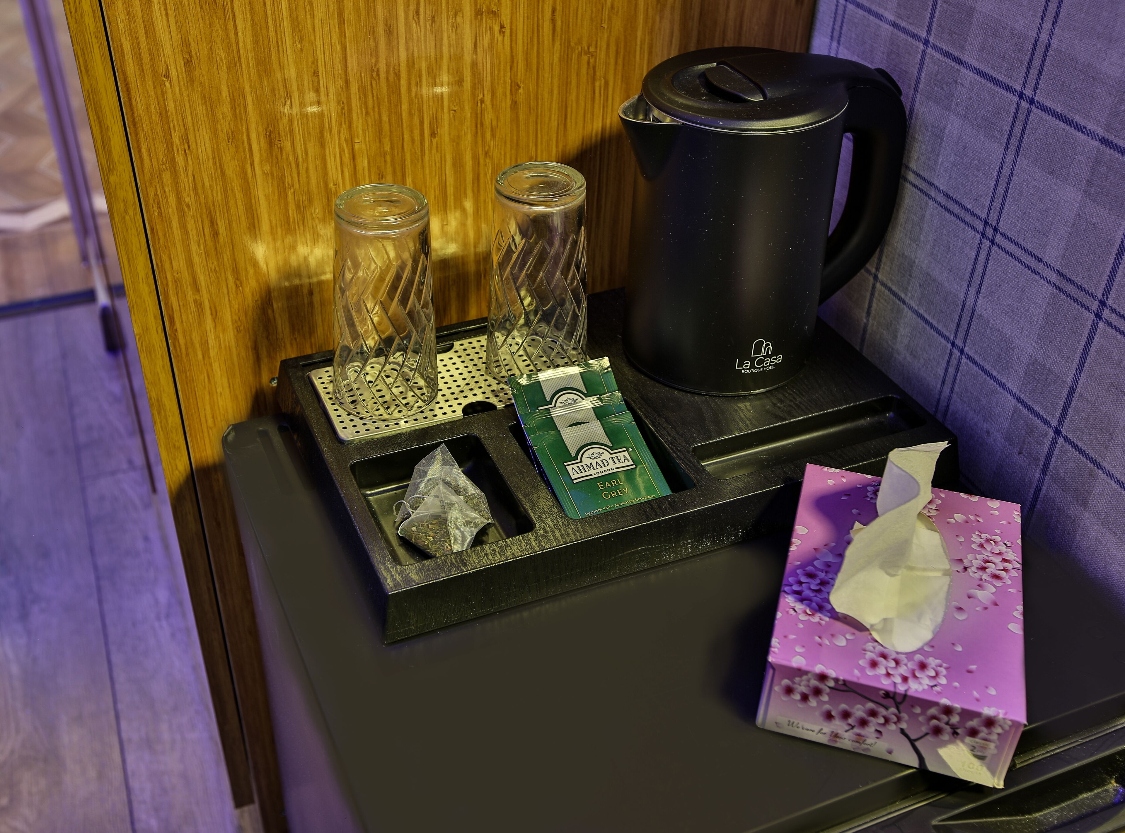 A black tray with a tea kettle, two glass containers, a tissue box, and a tissue.