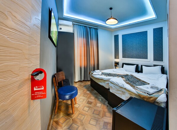 A hotel room with a bed, a chair, a desk, a ceiling light, and a window with curtains.