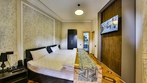 Una camera d'albergo con un letto grande, una TV fissata al muro e un pavimento in legno.