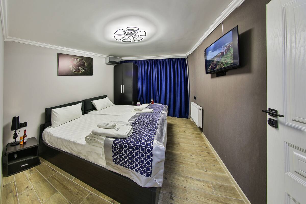 Ein Hotelzimmer mit einem großen Bett, einem Flachbildfernseher, einem Deckenventilator und einem Bild an der Wand.