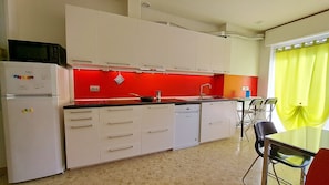 A compact kitchen with white cabinets, a red backsplash, a microwave, and a dining area with a table and chairs.