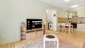 A modern living room with a flat-screen TV, wooden entertainment unit, and a dining area with a table and chairs.