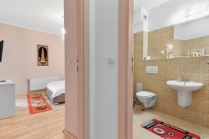 A hotel room with a bed, a small desk, a radiator, a bathroom with a sink and toilet, and a shower area. - Matteri (Sinaia)