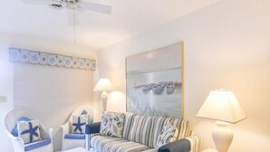 A living room with a striped sofa, a white armchair, a small table, and a ceiling fan. - 2 Bedroom 2 Bath outdoor pool (Ocean City)