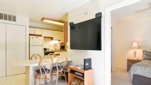 A compact room with a kitchenette, a dining area with chairs, a flat-screen TV mounted on the wall, a bed with a nightstand, and a lamp. - 2 Bedroom 2 Bath outdoor pool (Ocean City)