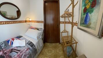 A bedroom with a bed, a wooden wardrobe, a mirror, a wall-mounted coat rack, and a framed painting.