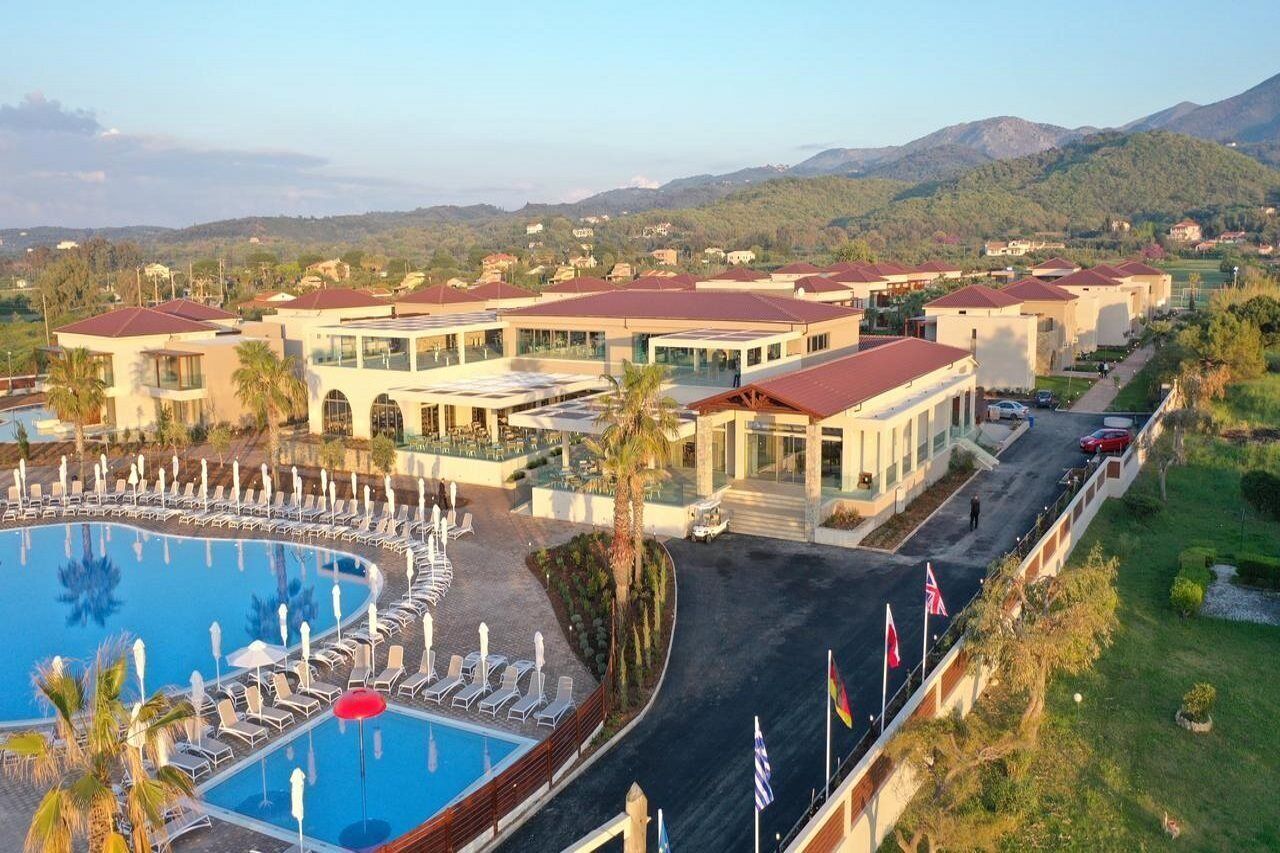 Un resort con piscina, varias construcciones y montañas al fondo.