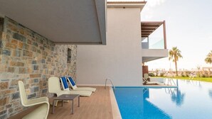 A modern pool area with lounge chairs and a stone wall. - Almyros Beach Resort & SPA (Corfu)