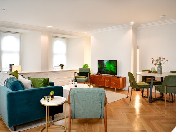 Ein modernes Wohnzimmer mit einer Couch, Sesseln, einem Couchtisch, einem Fernseher und einem Essbereich mit Tisch und Stühlen.