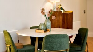 A round dining table with green upholstered chairs, a vase with flowers, and a lamp on the wall. - Beautiful 2 Bed Apartment with Parking in the Bay - Pass the Keys (Cardiff)