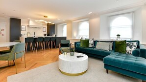 A modern living room with a teal sofa, a round coffee table, and a dining area with chairs. - Beautiful 2 Bed Apartment with Parking in the Bay - Pass the Keys (Cardiff)