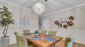 Ein Esszimmer mit Holztisch, grünen Polstersesseln, einer Topfpflanze und einer Pendelleuchte.