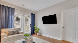 Ein Wohnzimmer mit einer Couch, einem Couchtisch, einem flachbildfernseher an der Wand und einer Tür.