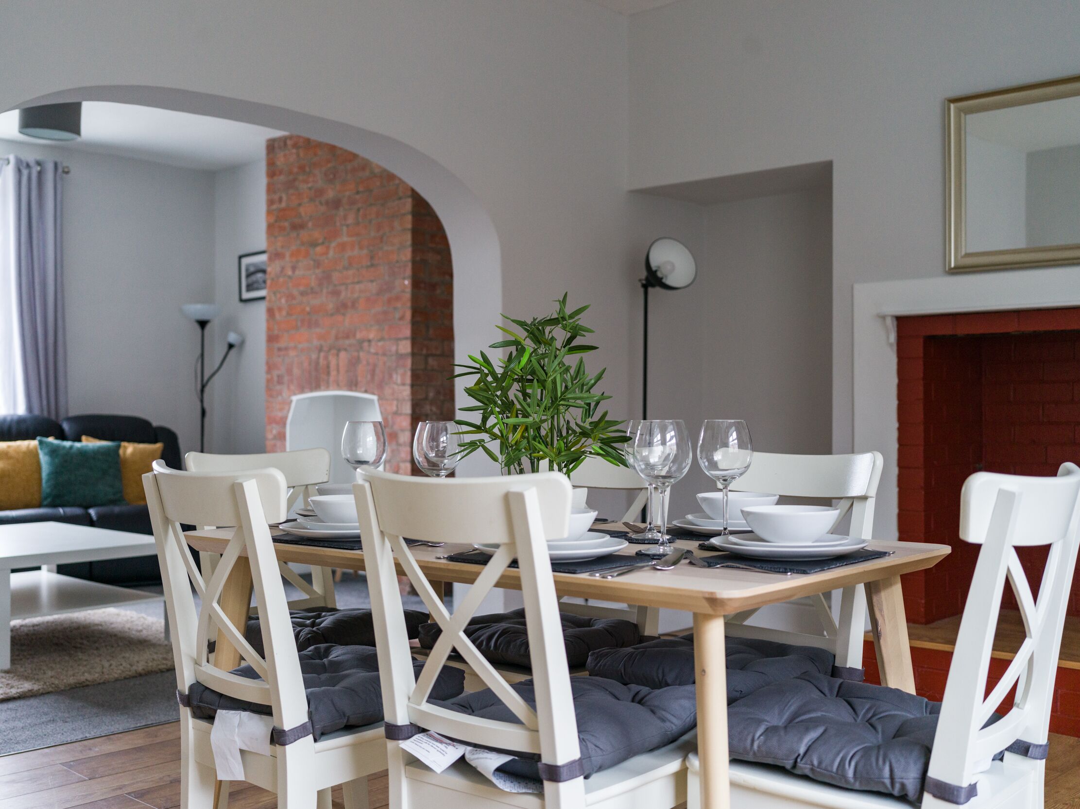 A dining area with a brick wall, white chairs, a table set with plates, glasses, and a potted plant.