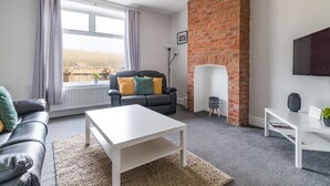 Un salon moderne avec une cheminée en briques, une table basse blanche, un canapé en cuir et une grande fenêtre avec des rideaux.