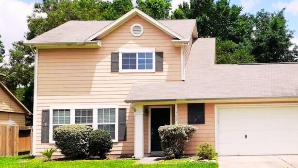 A two-story house with a garage, a front door, and a small front yard with two bushes. - Enjoy Vacation in a Quiet Area w/ Huge Backyard! (Crosby)