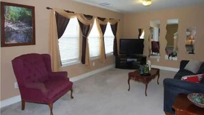 A living room with a red armchair, a blue sofa, a television, and a painting on the wall. - Enjoy Vacation in a Quiet Area w/ Huge Backyard! (Crosby)