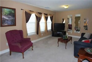 A living room with a red armchair, a blue sofa, a television, and a painting on the wall. - Enjoy Vacation in a Quiet Area w/ Huge Backyard! (Crosby)