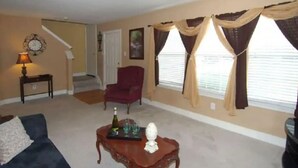A living room with a sofa, armchair, coffee table, and a staircase in the background. - Enjoy Vacation in a Quiet Area w/ Huge Backyard! (Crosby)
