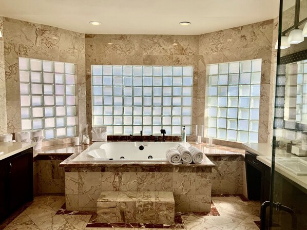 A modern bathroom with a large marble bathtub, frosted glass windows, and a marble floor.