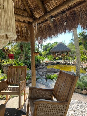 A wooden gazebo with a thatched roof, surrounded by lush greenery and a small pond. - Maui Mansion Miami w/resort pool (Southwest Ranches)