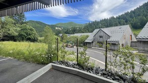 Paesaggio rurale con una strada, edifici in legno e una collina boscosa sullo sfondo.