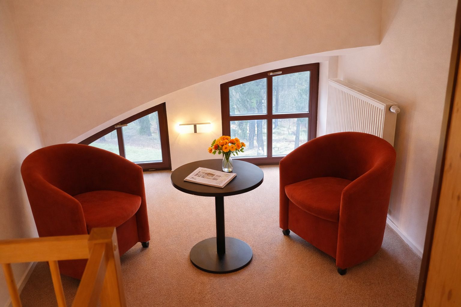 Una habitación con dos sillas rojas, una mesita con un florero y una ventana con vistas a árboles.