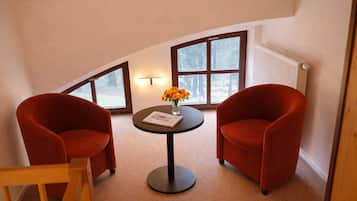 A room with two red chairs, a small table with a vase of flowers, and a window with a view of trees.