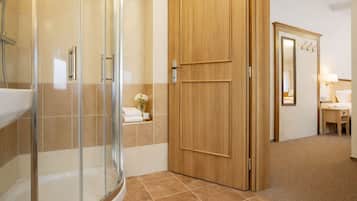 A hotel bathroom with a glass shower enclosure, a wooden door, and a mirror with hooks.