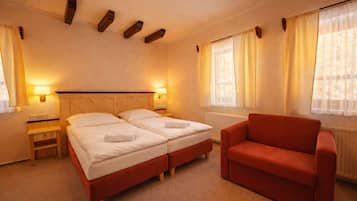 A hotel room with two beds, a red armchair, bedside lamps, and a window with curtains.