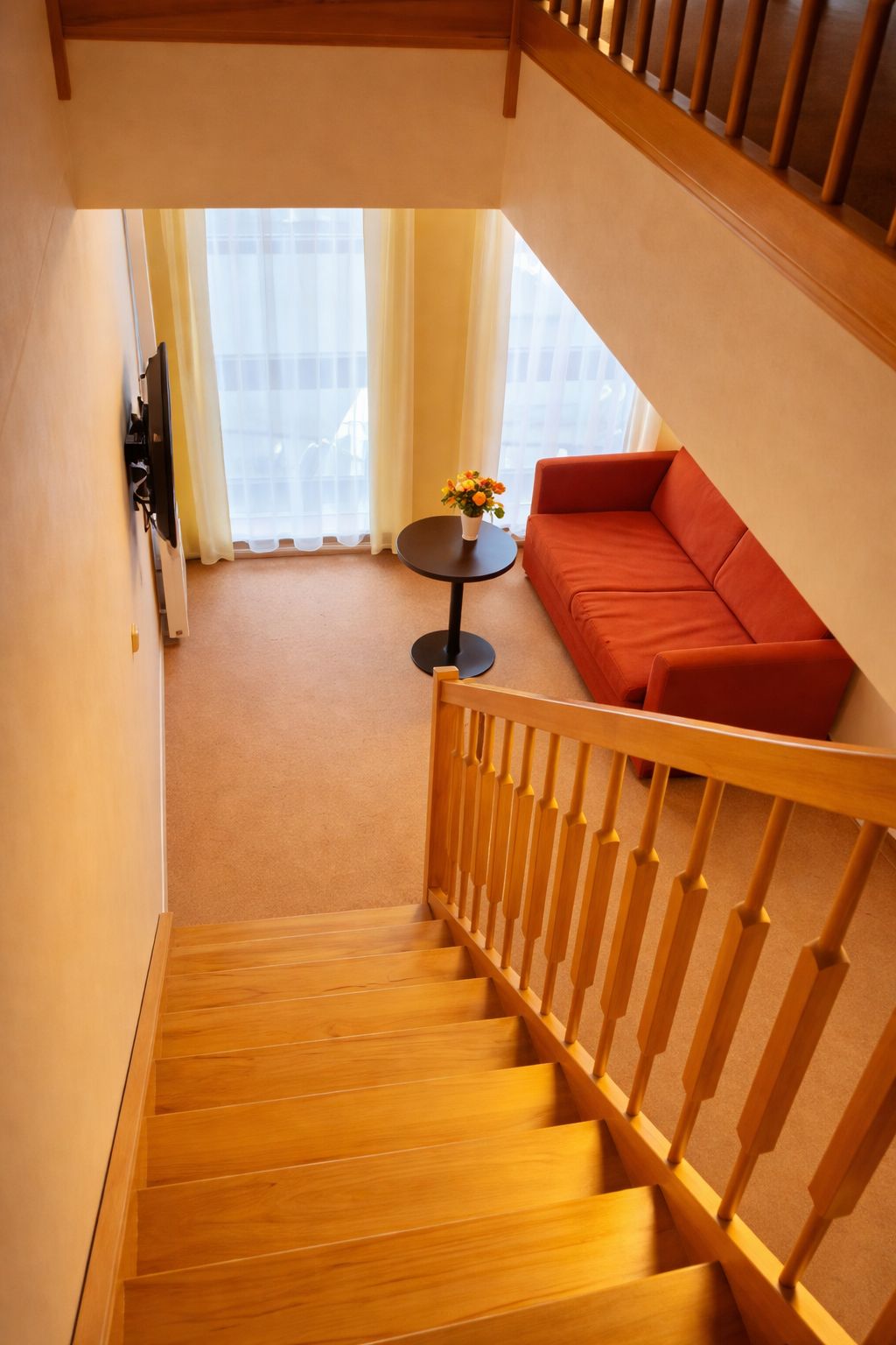 Eine Treppe führt zu einem Wohnbereich mit einem roten Sofa und einem kleinen runden Tisch mit Blumen.