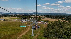 A ski lift with passengers, surrounded by open fields and distant mountains. - Hotel Obří Sud (Dlouhý Most)