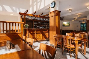 A restaurant with wooden furniture, a bar area, and a clock on the wall. - Hotel Obří Sud (Dlouhý Most)