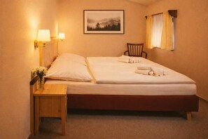 Ett hotellrum med en säng, två sänglampor, en stol, en tavla på väggen och ett fönster med gardiner.