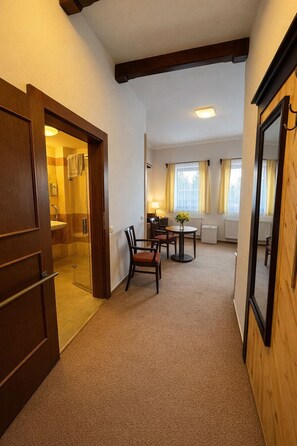 A hotel room with a wooden door, a small dining area with a table and chairs, a window with curtains, and a radiator. - Hotel Obří Sud (Dlouhý Most)